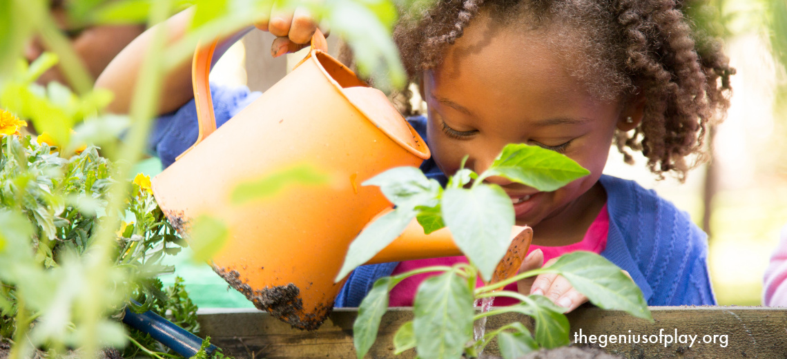 young African American girl smiling and holding watering can to water plants in a garden