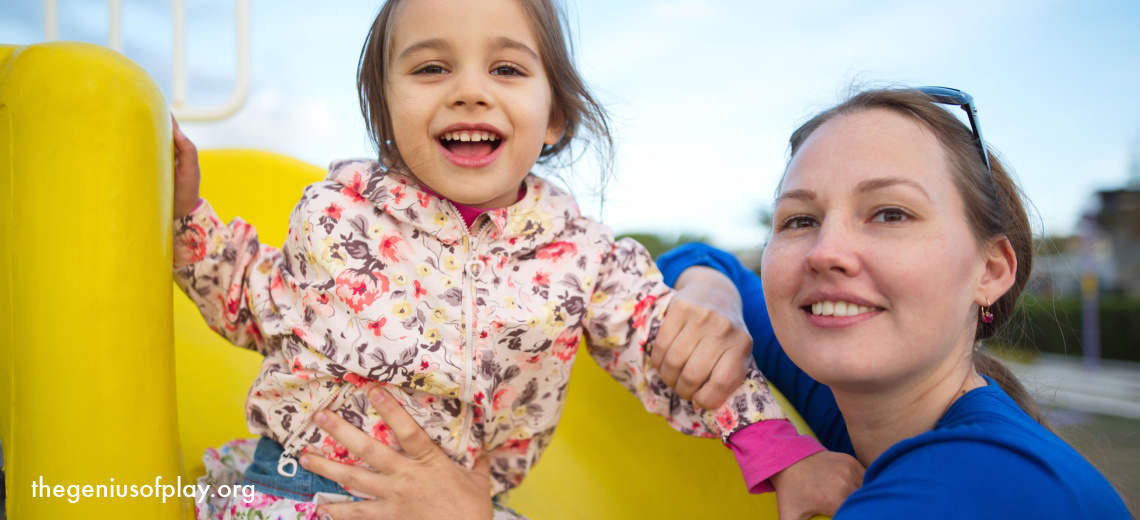 happy Caucasian mom and young toddler daughter sitting on a slide at a playground