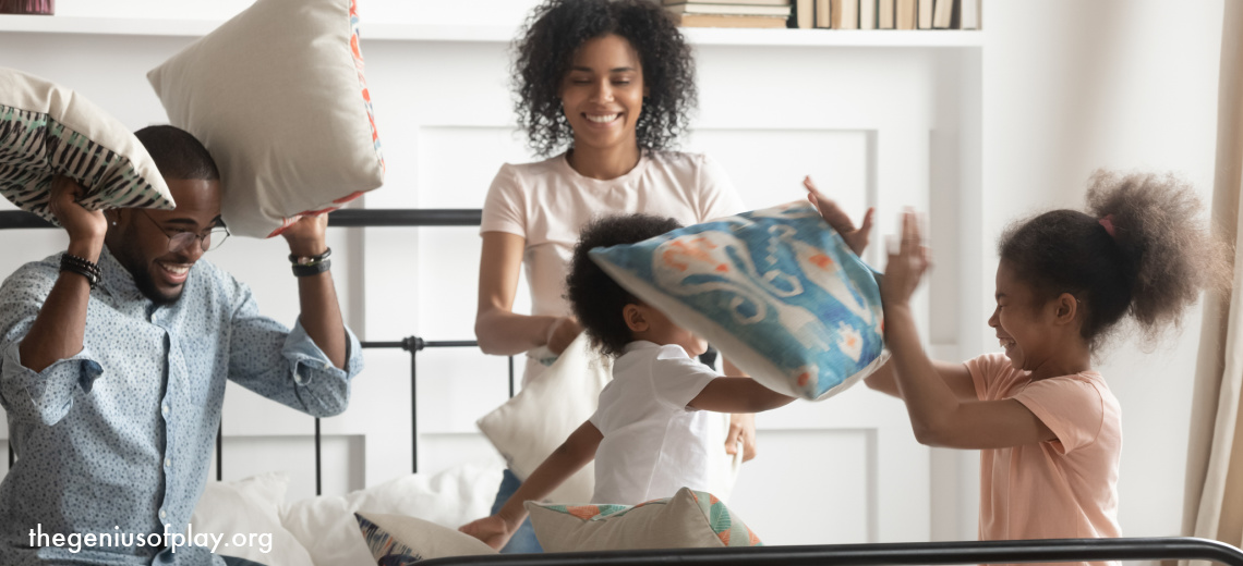 African American mom and dad having a pillow fight with their young son and daughter on top of a bed