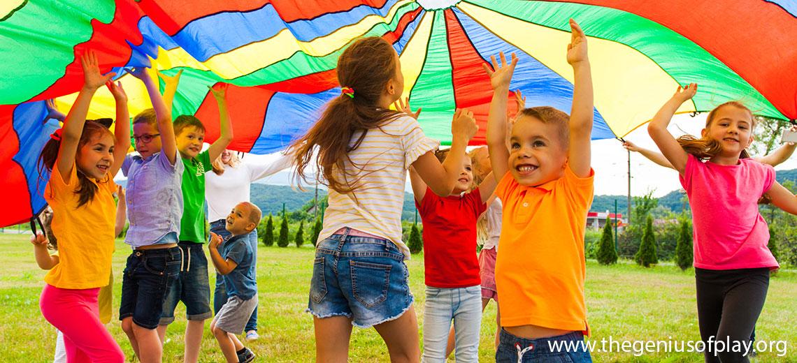 group of pre-school kids playing under a colorful parachute outdoors
